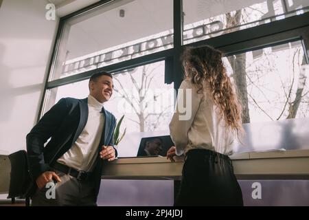 Two business colleagues talking while standing next to the windows of the co working space Stock Photo