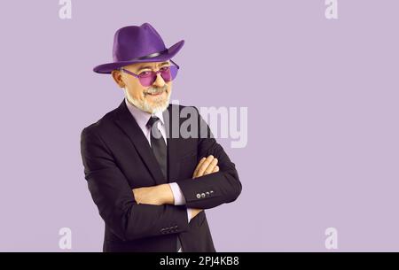 Happy senior man in suit, purple fedora hat and purple glasses isolated on lilac background Stock Photo