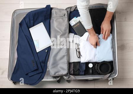 Man packing suitcase for business trip on wooden floor, top view Stock Photo