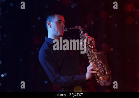 Young man playing saxophone on dark background. Bokeh effect Stock Photo