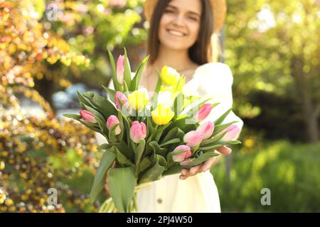 Beautiful young woman with bouquet of tulips in park, focus on flowers Stock Photo