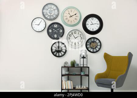 Armchair, console table and many different clocks hanging on white wall in room Stock Photo