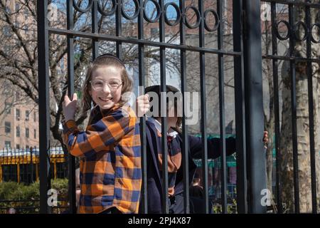 A Hasidic jews boy enjoys swinging on a fence door during recess from his Yeshiva. In Brooklyn, New York. Stock Photo