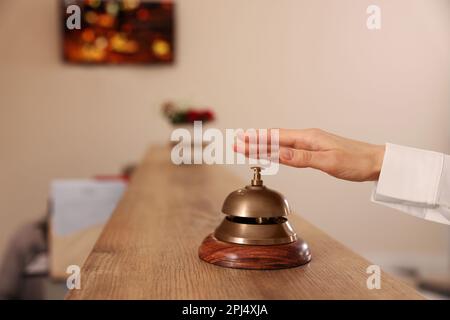 Woman ringing hotel service bell at wooden reception desk, closeup Stock Photo