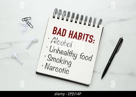 Notebook with list of bad habits and pen on white marble table, flat lay. Change your lifestyle Stock Photo