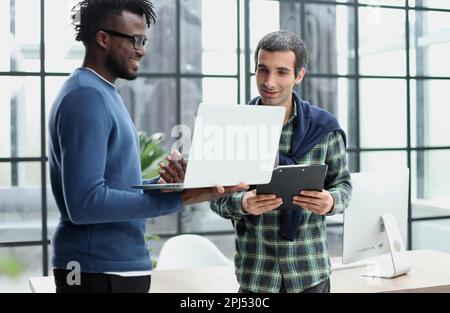 young business men standing together holding a laptop, discussing business Stock Photo