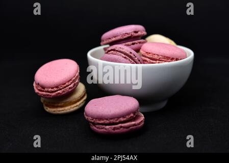 Macaroons in a white plate on a black background. Macaroons in a ceramic bowl. Colorful sweet cookies. Stock Photo