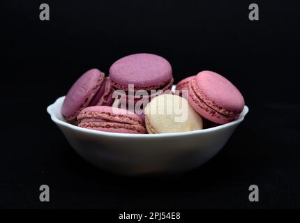 Macaroons in a white plate on a black background. Macaroons in a ceramic bowl. Colorful sweet cookies. Stock Photo