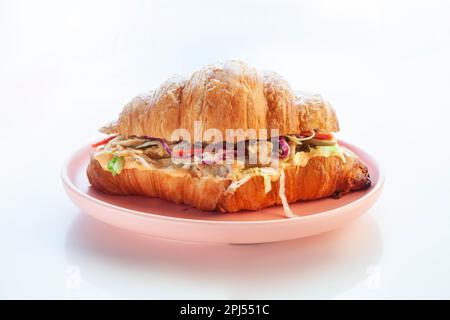 Brioche croissant chicken sandwich on a pink plate white background. Stock Photo