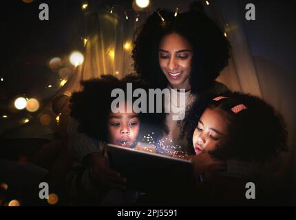Tablet, night a mother reading to her kids in a tent while camping in the bedroom of their home together. Black family, story or children with a woman Stock Photo
