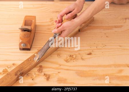 Top view of body part of anonymous carpenter carving wood on plank with chisel on workbench near jack plane while working with lumber in workroom Stock Photo