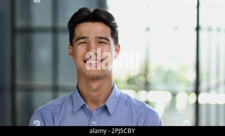 Well dressed young Asian businessman smiling confidently while standing alone in a bright modern office Stock Photo