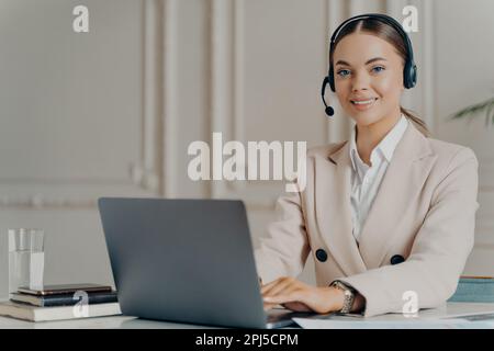 Cheerful female customer support operator working on computer in modern call center office, happy business woman smiling at camera while sitting at he Stock Photo