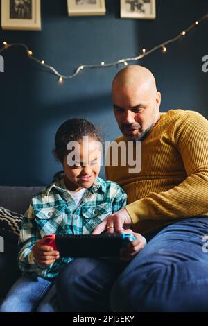 Boy with Down syndrome playing computer game, father helping Stock Photo
