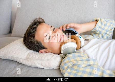 Adorable cute boy using smartphone lying on sofa at home Stock Photo