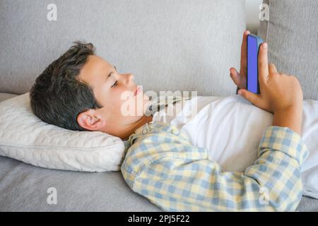 Adorable cute boy using smartphone lying on sofa at home Stock Photo