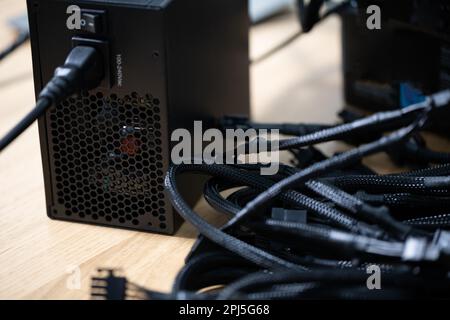 Tangled black computer cables lying on a brown wooden table Stock Photo