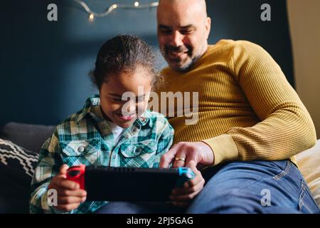 Boy with Down syndrome smiling and playing computer game with father Stock Photo