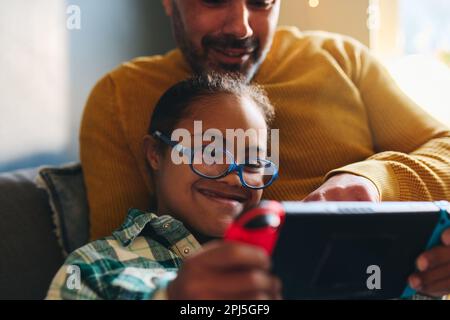 Boy with Down syndrome smiling and playing computer game with father Stock Photo