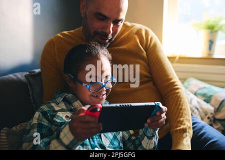 Cheerful boy with Down syndrome playing computer game with his father Stock Photo