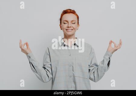 Young redhaired woman meditating in a green sweater against a purple ...