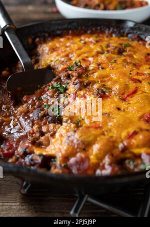 Bean stew alla chili con carne with cheddar cheese topping in a cast iron pan Stock Photo
