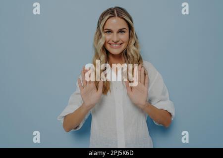 Young woman politely refusing what she is offered, both her hands in front of her, showing her disagreement with gesture while standing alone next to Stock Photo