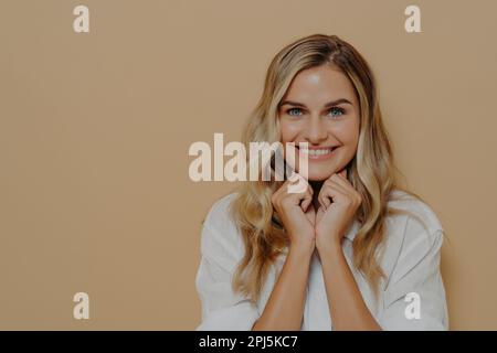 Close up shot of cute dreamy young female daydreaming, making up plan in mind and smiling delighted, keeping hands folded under chin and looking slyly Stock Photo