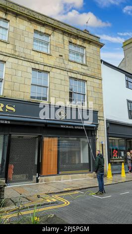 A man using a water fed telescopic window cleaning pole, on a street in Truro, Cornwall, England, UK Stock Photo