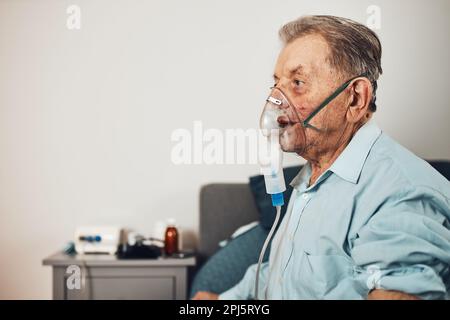 Senior man inhaling airways and lungs applying medicine. Covid-19 or coronavirus treatment. Man breathing through face mask using nebuliser Stock Photo