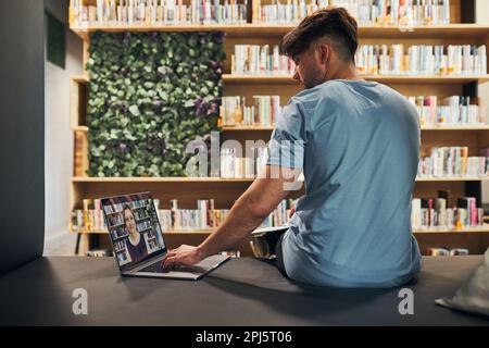 Student learning in university library. Young man having video class on laptop. Man listening to online course. Focused student studying for college e Stock Photo