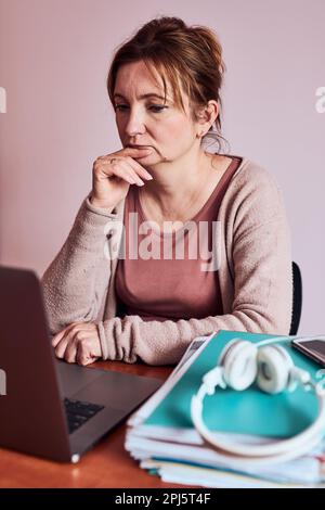 Woman focused on her work working hard doing her job remotely on laptop from home. Woman sitting at desk in front of computer looking at screen. Conce Stock Photo