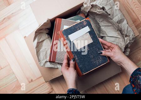 Woman taking books out of cardboox. Unpacking parcel. Female hands holding books Stock Photo