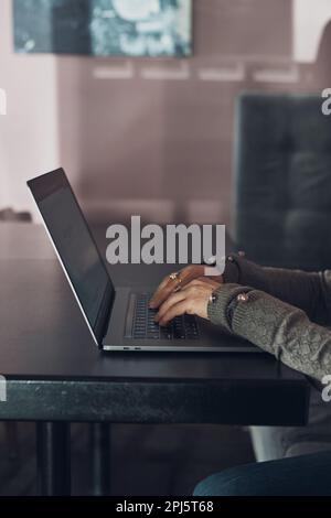 Woman working remotely on her laptop computer managing her work sitting at the table in a cafe. Female hands typing on laptop keyboard Stock Photo