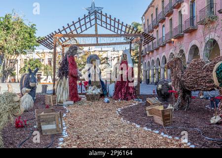 Public square with Christmas representation of nativity scene against blue sky, figures with virgin mary, joseph, baby jesus and animals, building in Stock Photo