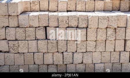 Group of stacked grayish bricks forming a wall, illuminated by sunlight, rough and cracked texture, material used in construction industry Stock Photo