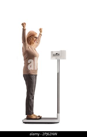 Full length side shot of a happy woman weighing on a medical scale and gesturing happiness isolated on white background Stock Photo