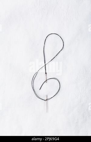 Macro of sewing needle in white fabric in violin key shape. Concept of handcraft and art Stock Photo