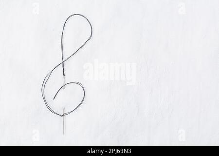 Macro of sewing needle in white fabric in violin key shape. Concept of handcraft and art. Copy space for your text Stock Photo