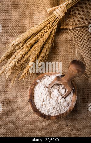 Flour in wooden bowl with grain on burlap background Stock Photo