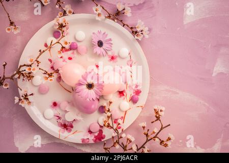 Pink Easter eggs with blooming branch, flowers and sweets for Easter and spring Stock Photo