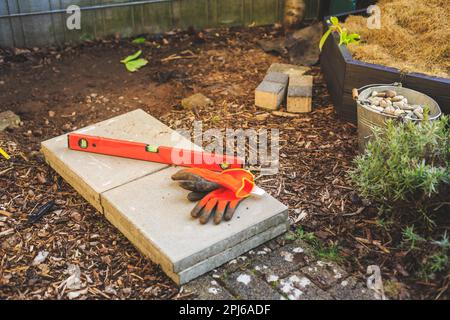 Building garden path or base in garden, spirit level, working gloves and concrete slabs Stock Photo