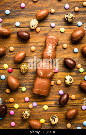 Chocolate Easter bunny with sweet chocolate eggs and colorful sweets on wooden background Stock Photo