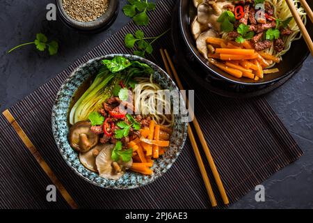 Asia style ramen soup with udon noodle, beef, shiitake, pak choi cabbage and carrots on black background Stock Photo