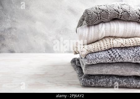 Stack of cozy knitted sweaters and pullovers on wooden background. Autumn and winter concept Stock Photo