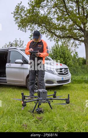 Rescue team operating professional drone to locate roe deer fawns hidden in grass with thermal imaging camera before mowing grassland in spring Stock Photo