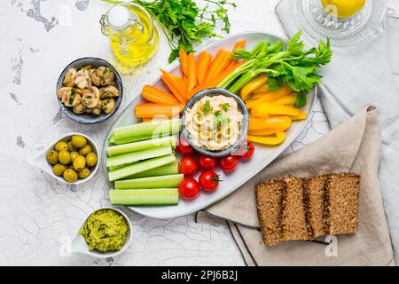 Platter of assorted fresh vegetables with avocado dip, hummus, marinated mushrooms and olives Stock Photo