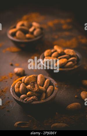 Organic cocoa beans in small bowls on brown background. Baking and cooking ingredients Stock Photo