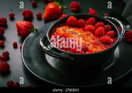 Breakfast red smoothie bowl with chia seeds, strawberry, raspberry and redcurrants on black background Stock Photo