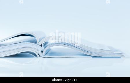 Stack of open magazines in blue tone on white background with copy space Stock Photo